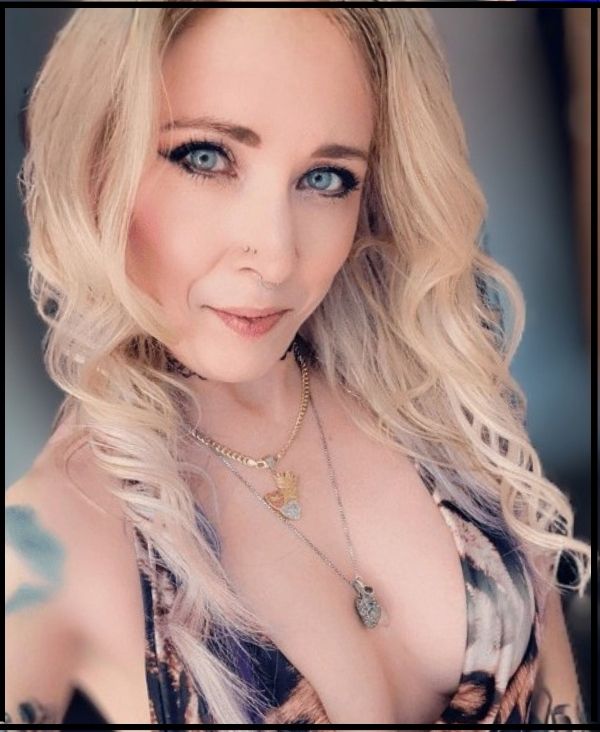 Goddess Jessica Jade with piercing blue eyes and soft blonde curls, holding calm, direct eye contact