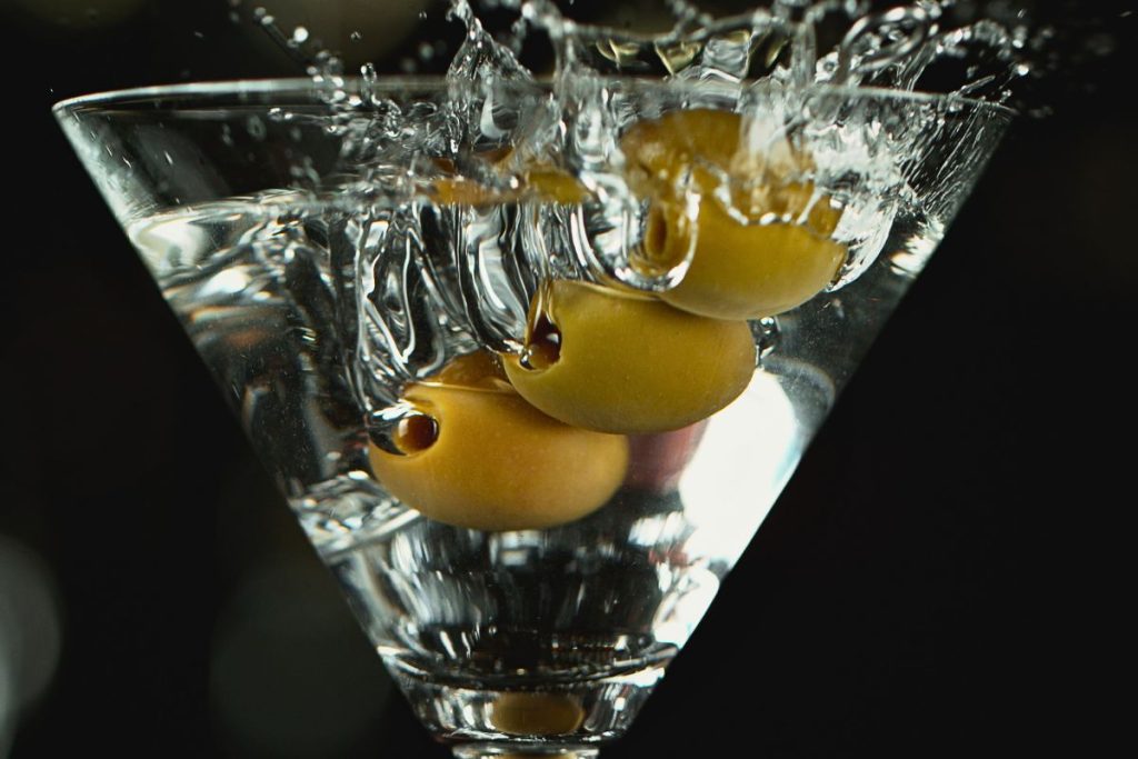 Dirty martini with olives splashing in glass, close-up.